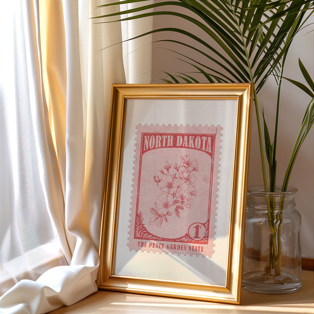 North Dakota stamp print in a gold frame leaning by a cream curtain with a palm in a glass jar