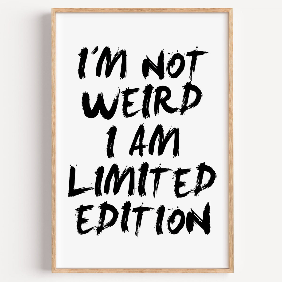 I'm not weird brush lettering quote print in a light oak frame on a plain white wall