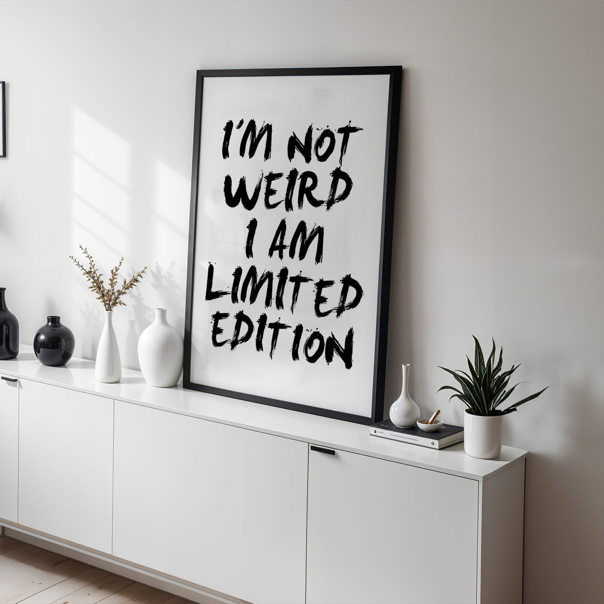 I'm not weird brush lettering quote print in a black frame on a white sideboard with black and white vases