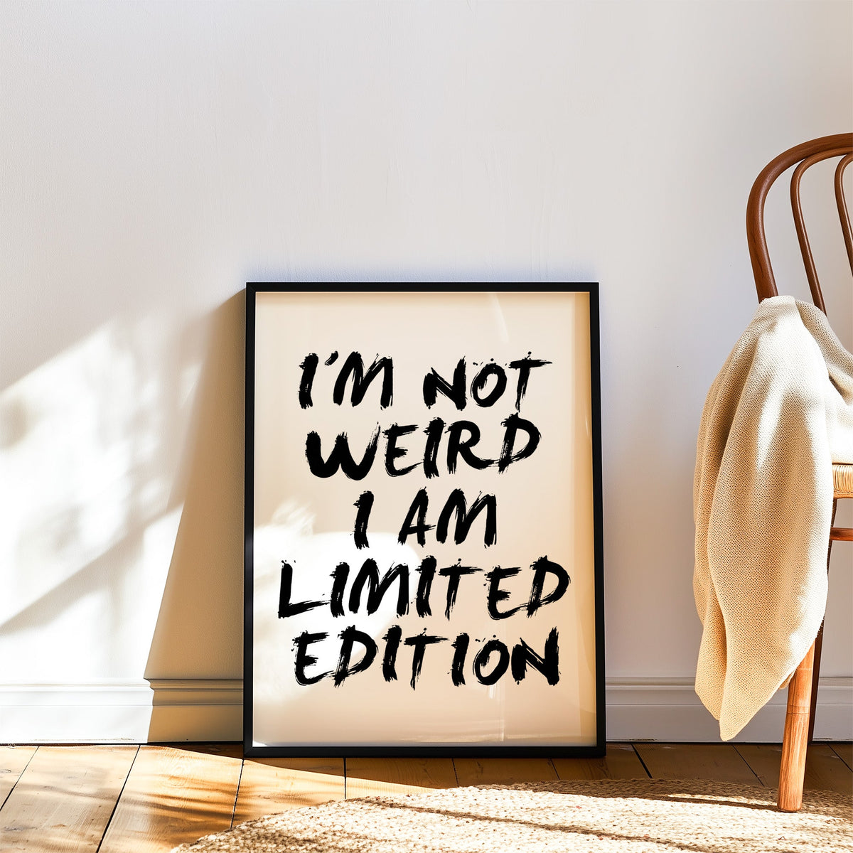 I'm not weird brush lettering quote print in a black frame leaning on a wood floor beside a bentwood chair