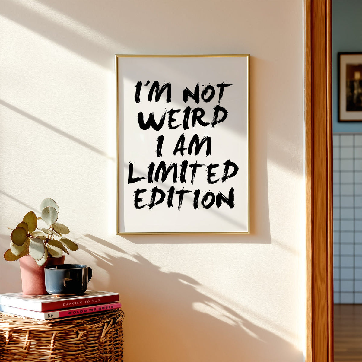 I'm not weird brush lettering quote print shown in a gold frame above a wicker basket and stacked books