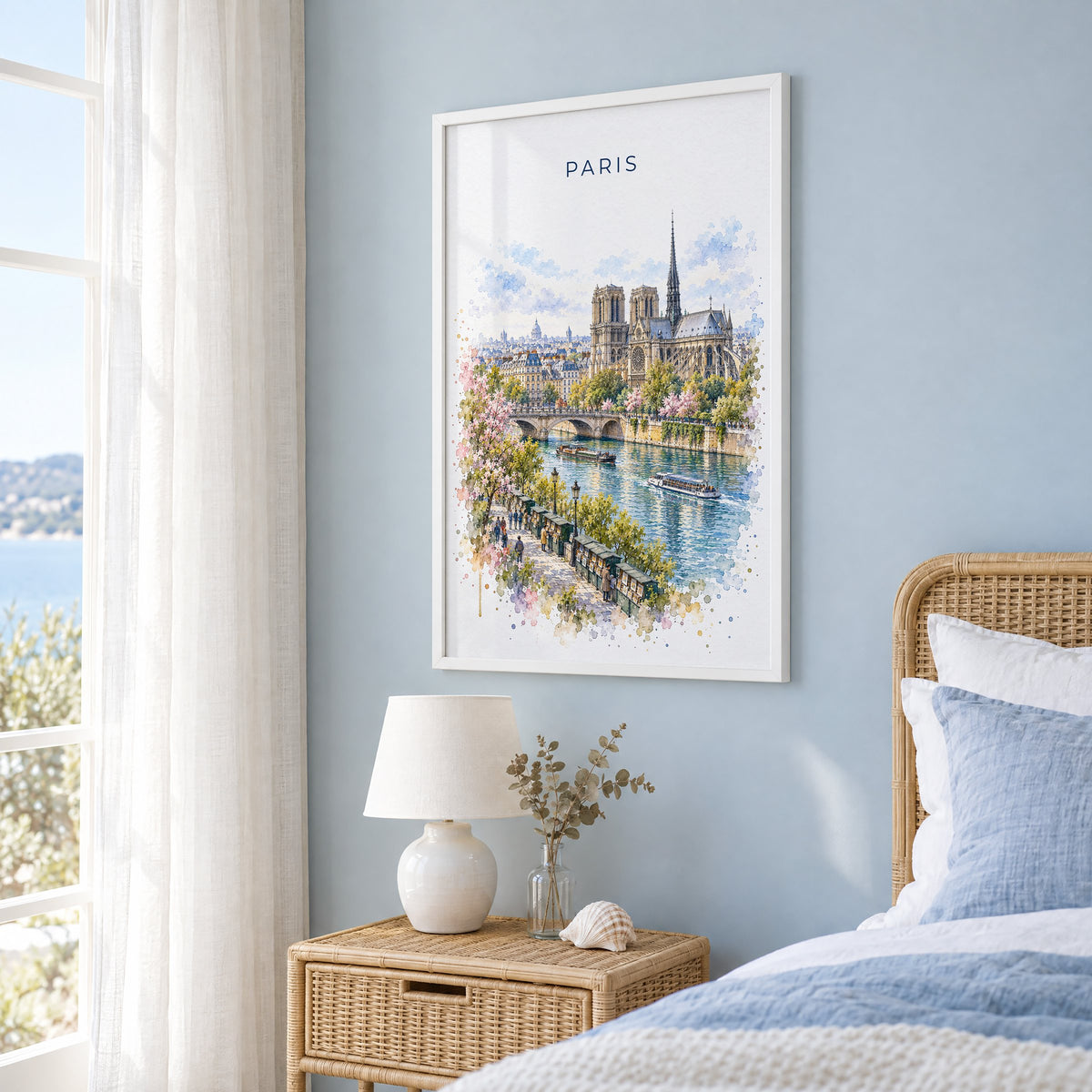 Notre-Dame Paris watercolor print in a white frame on a pale blue wall beside a rattan bed in a coastal bedroom