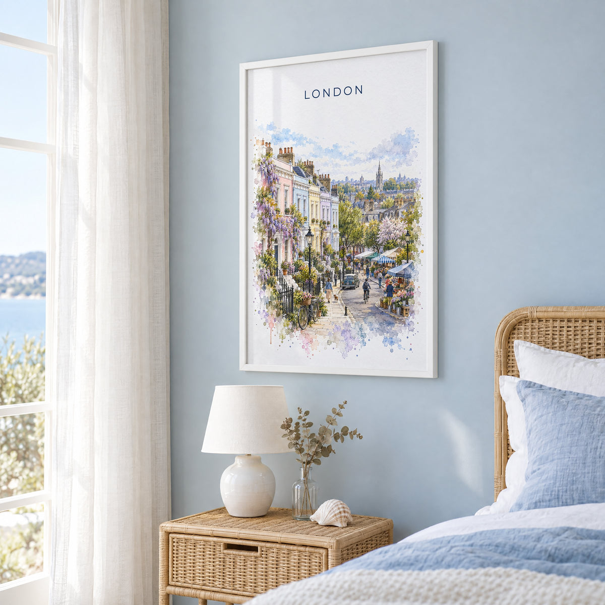 Notting Hill London watercolor print in a white frame on a pale blue wall beside a rattan bed in a coastal bedroom