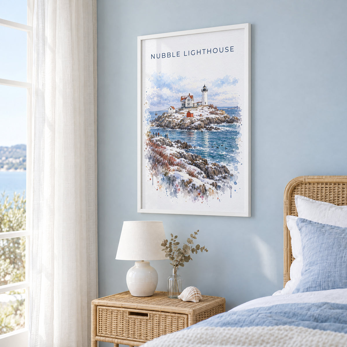 Nubble Lighthouse watercolor print in a white frame on a pale blue wall beside a rattan bed in a coastal bedroom