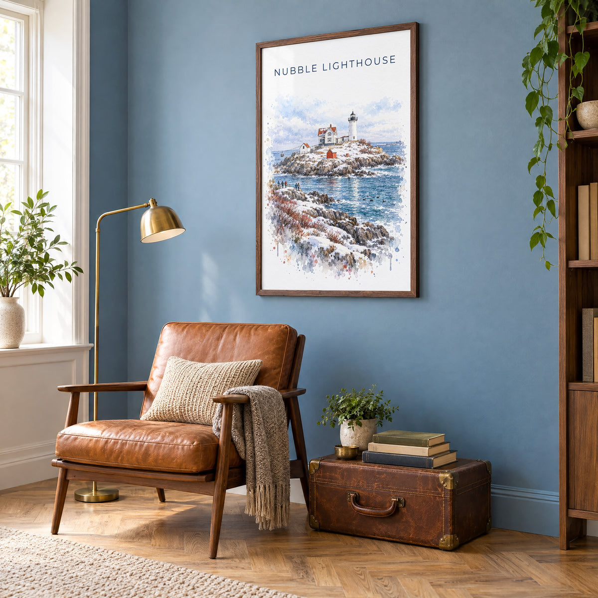 Nubble Lighthouse watercolor print in a walnut frame on a blue wall above a leather armchair in a reading nook