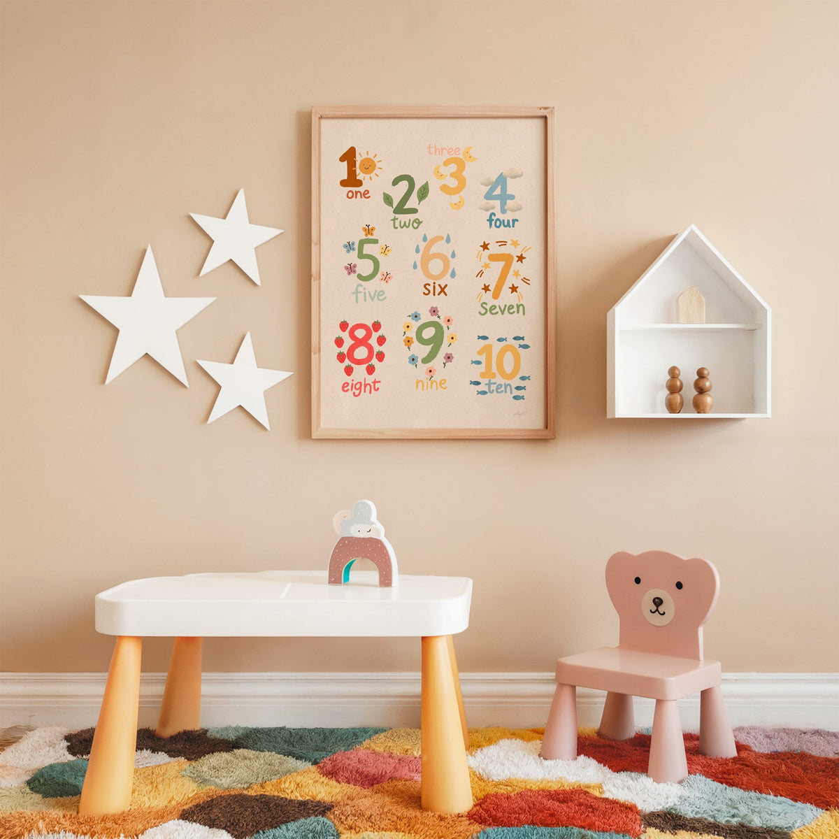 Numbers one to ten counting chart nursery print in an oak frame on a peach wall above a kids table with wall stars