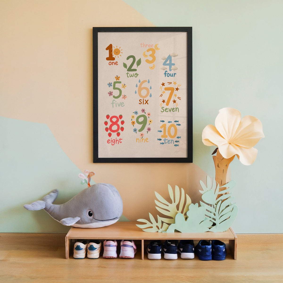 Numbers one to ten counting chart nursery print in a black frame on a mint and peach wall above a whale plush