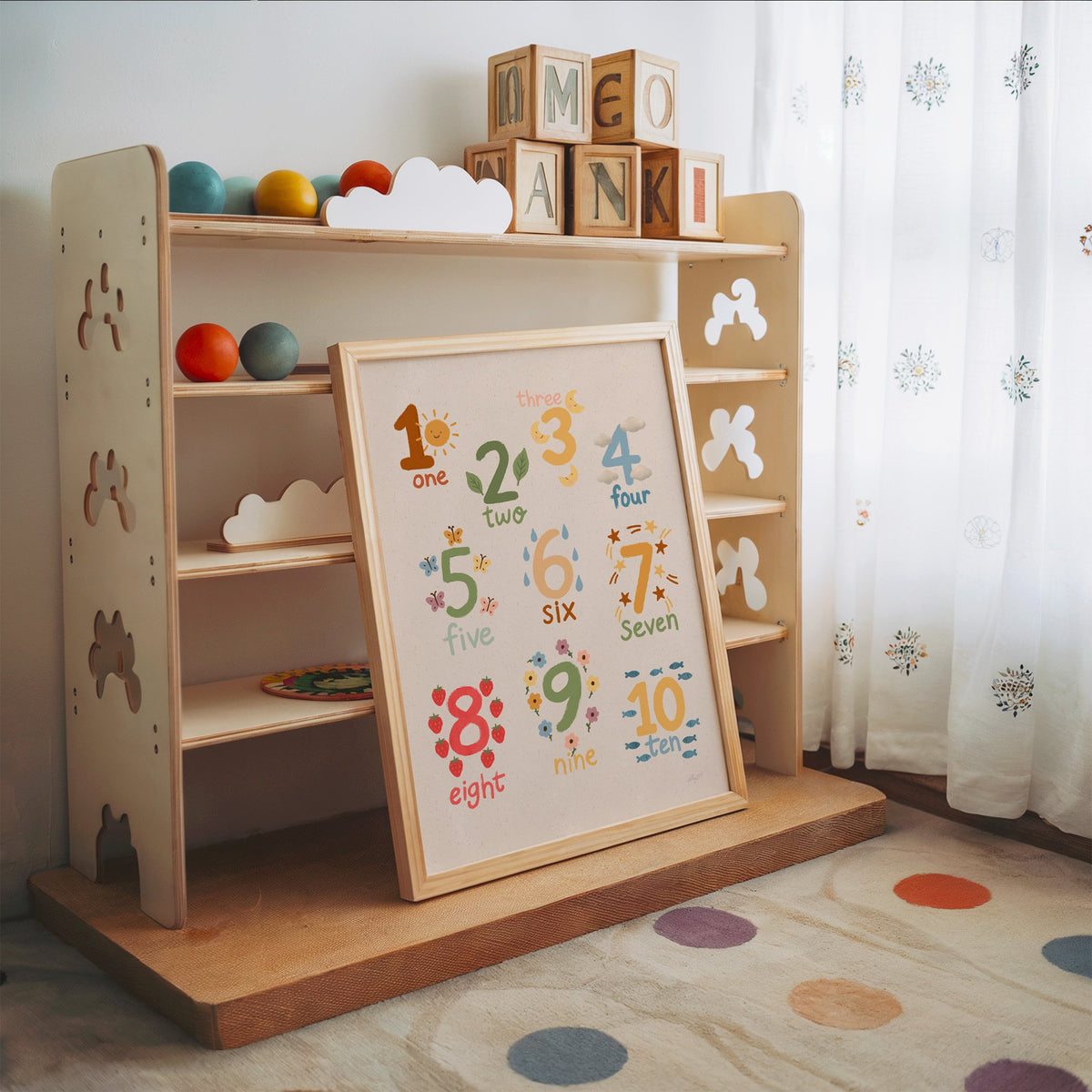 Numbers one to ten counting chart nursery print in an oak frame leaning on a toy shelf with wooden letter blocks