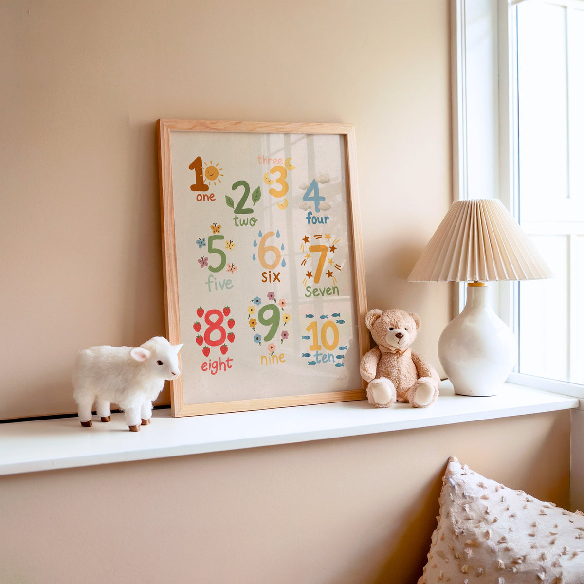 Numbers one to ten counting chart nursery print in an oak frame on a window ledge with a toy lamb and teddy
