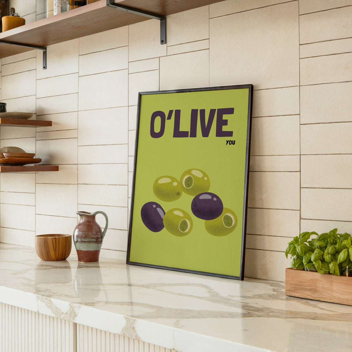 O Live You olives print in a black frame leaning on a marble counter in a tiled kitchen