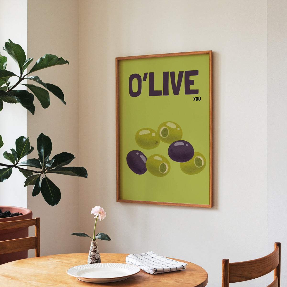 O Live You olives print in a walnut frame above a round table beside a fiddle-leaf fig