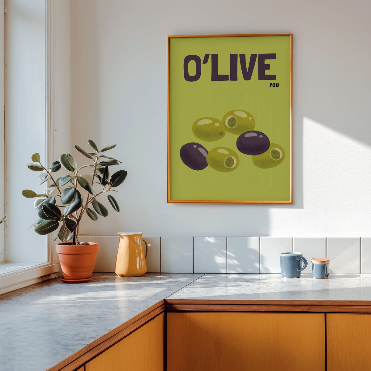 O Live You olives print shown in a gold frame above a marble counter in a tan kitchen