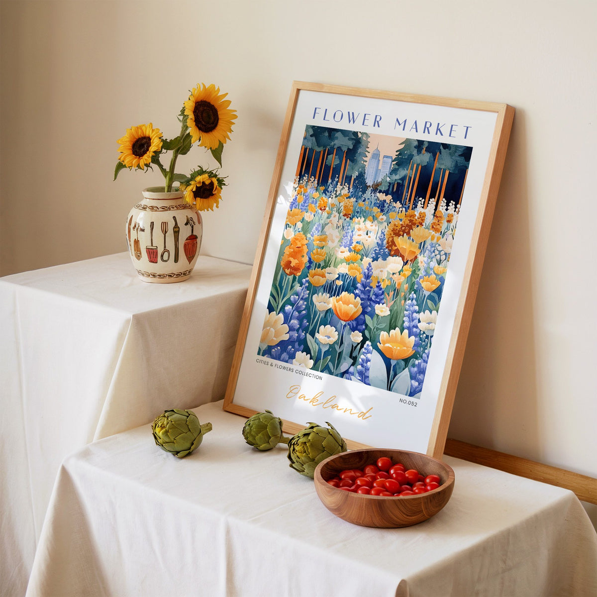 Oakland flower market print in an oak frame leaning on a linen-draped table beside a vase of sunflowers