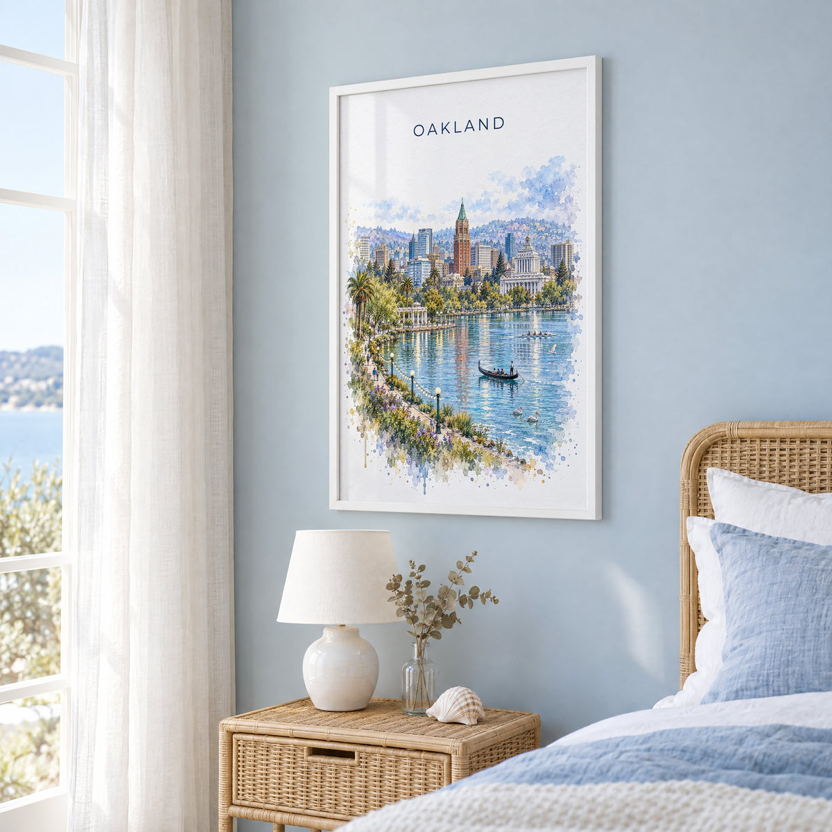 Oakland watercolor print in a white frame on a pale blue wall beside a rattan bed in a coastal bedroom