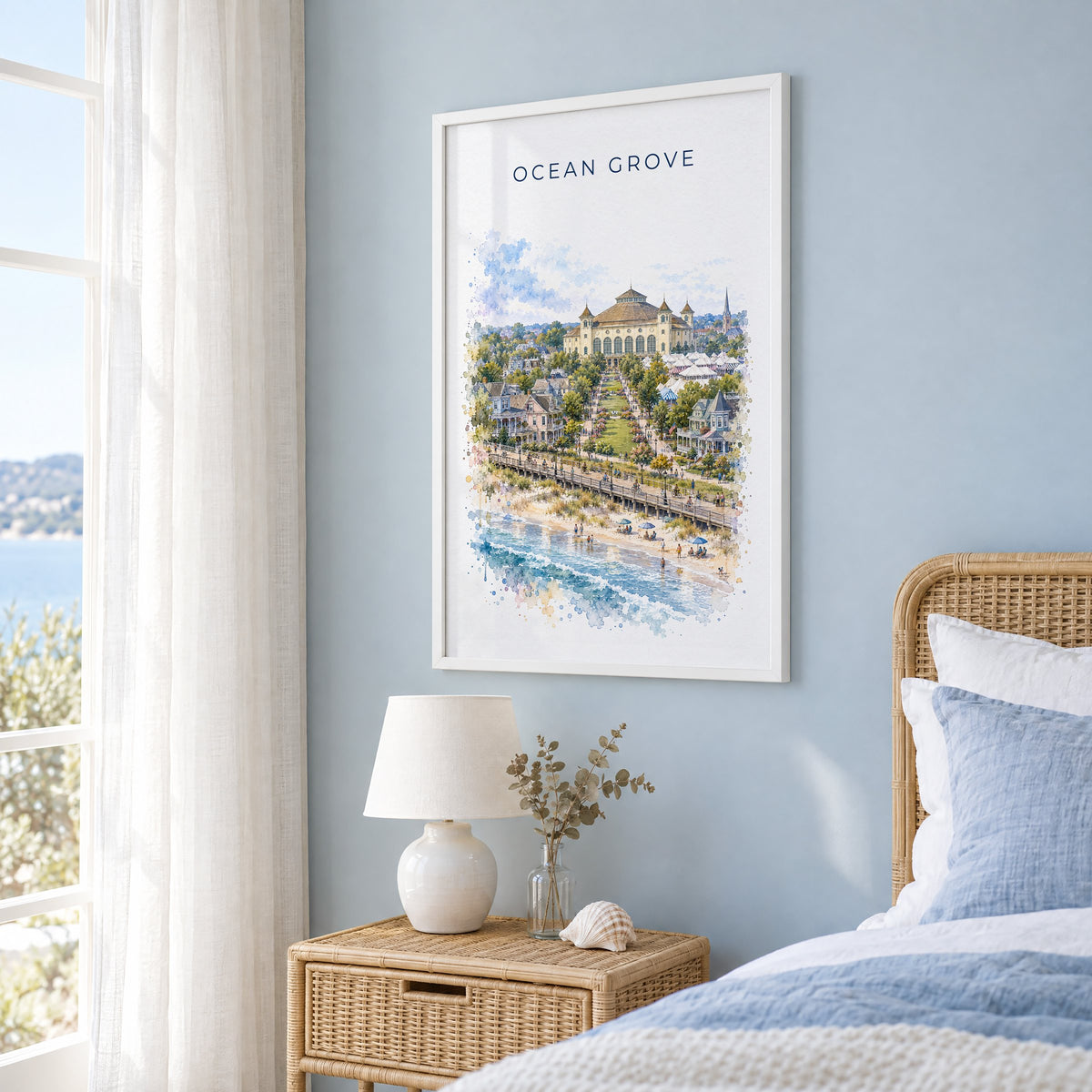 Ocean Grove, New Jersey watercolor print in a white frame on a pale blue wall beside a rattan bed in a coastal bedroom