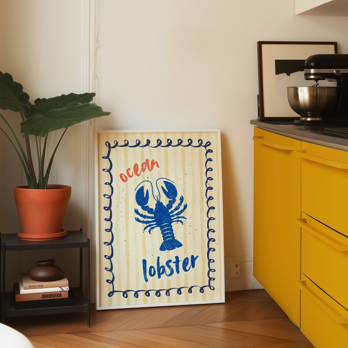 Blue lobster print in a white frame leaning on parquet beside a bright yellow kitchen