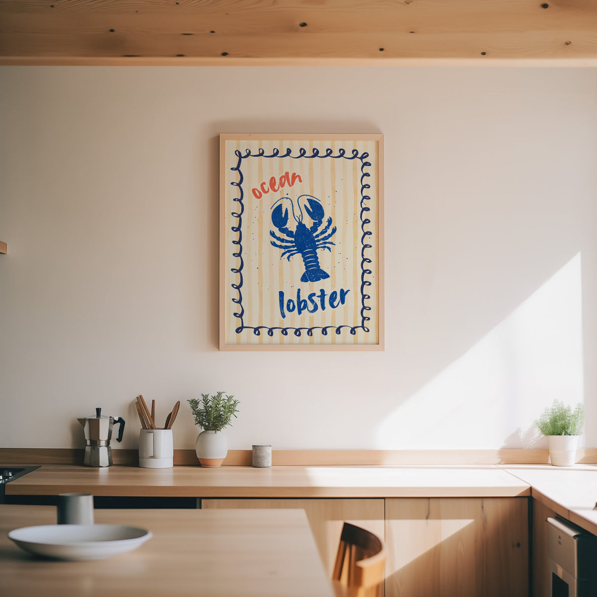 Blue lobster print in an oak frame above a wood counter with a moka pot and herbs