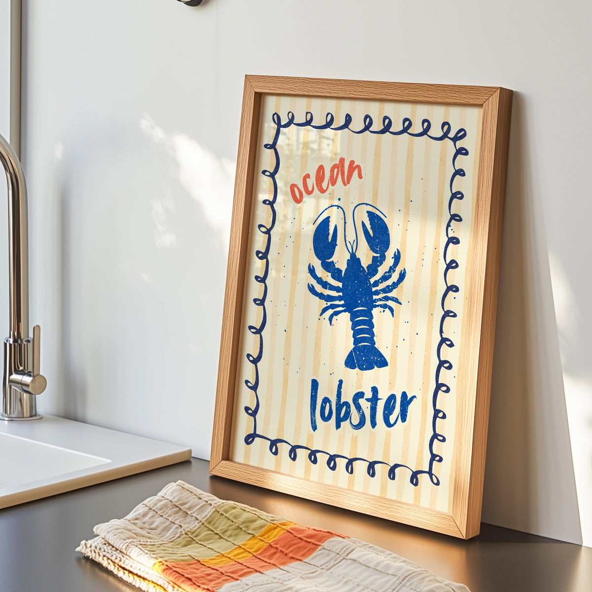 Blue lobster print in an oak frame by the kitchen sink beside a striped tea towel