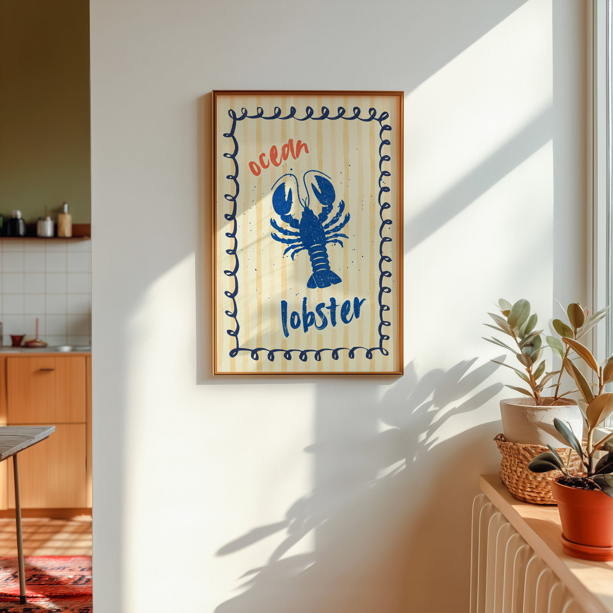 Blue lobster print shown in a gold frame in sunlight with plants and a kitchen beyond
