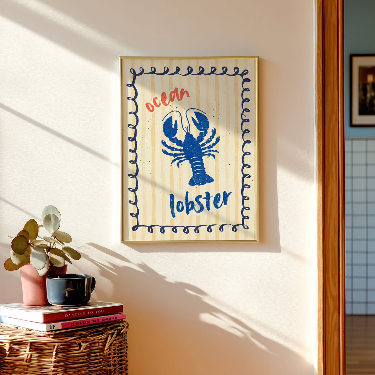 Blue lobster print shown in a gold frame above a basket of books and a pilea plant