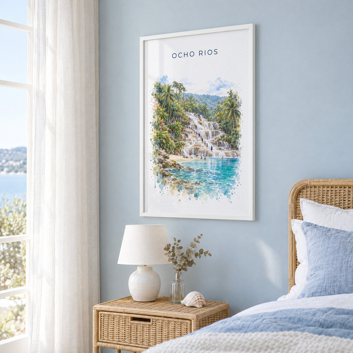 Ocho Rios watercolor print in a white frame on a pale blue wall beside a rattan bed in a coastal bedroom