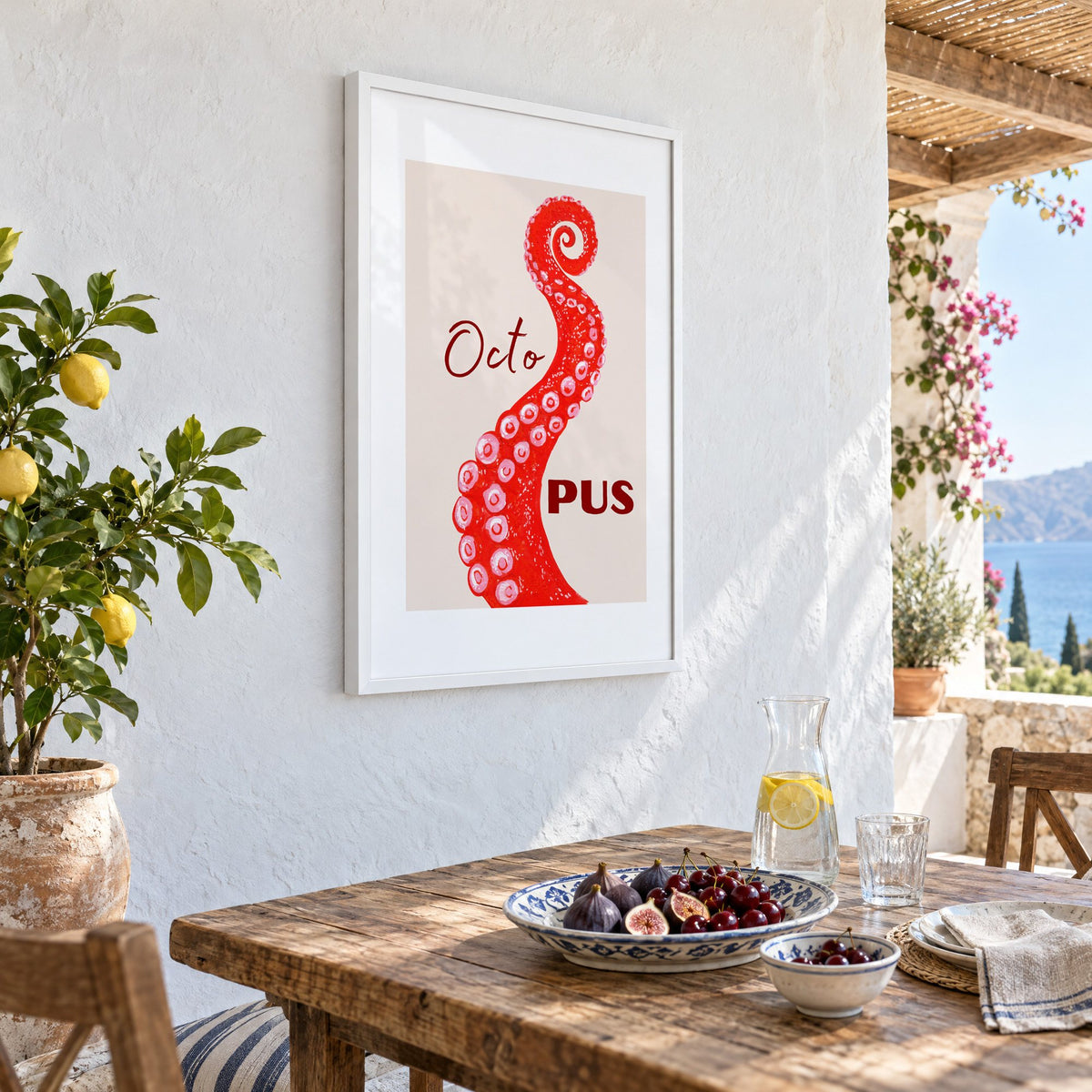 Octo PUS red gouache octopus tentacle print in a white frame on a whitewashed terrace wall above a lunch table with figs and cherries, seen at an angle