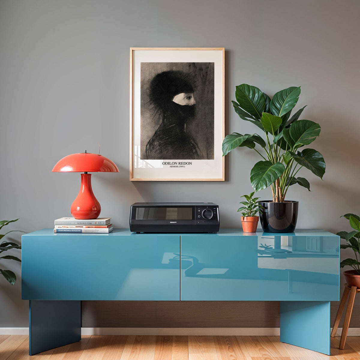 Redon charcoal print in an oak frame above a teal sideboard with a red lamp