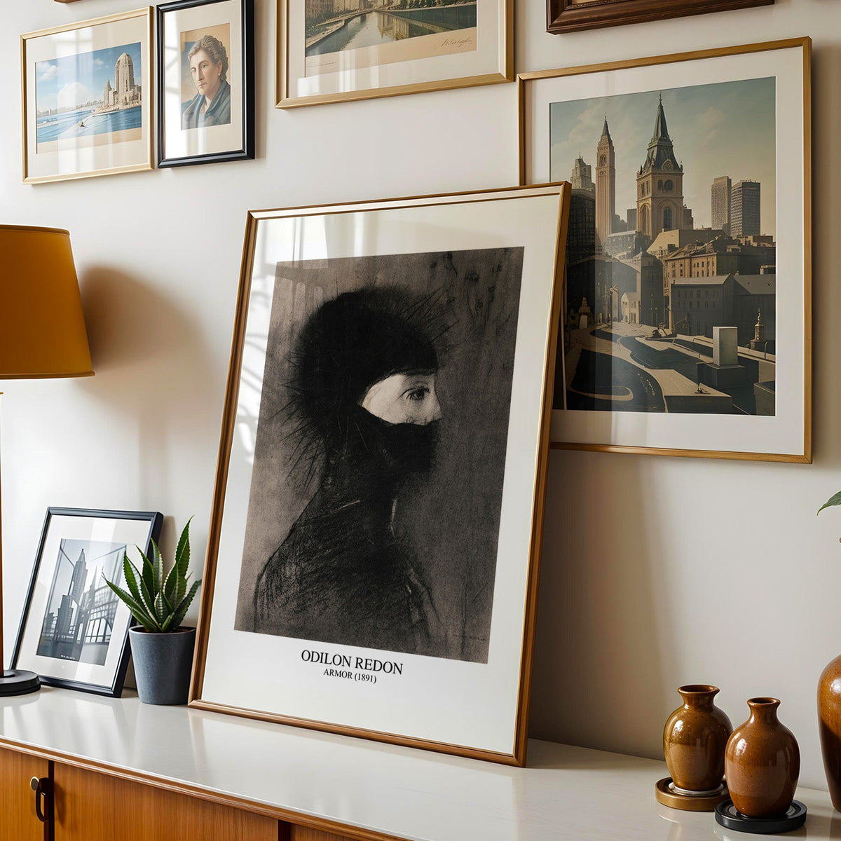 Black and grey charcoal print shown in a gold frame leaning on a sideboard in a gallery wall