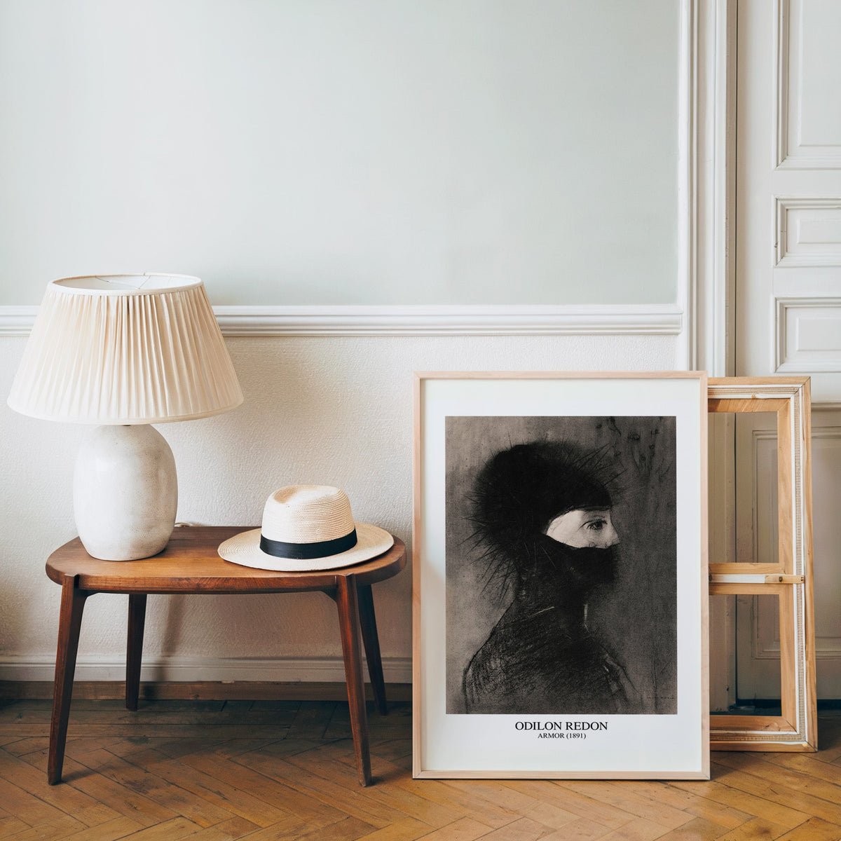 Symbolist charcoal poster in a light wood frame leaning by a bench and hat