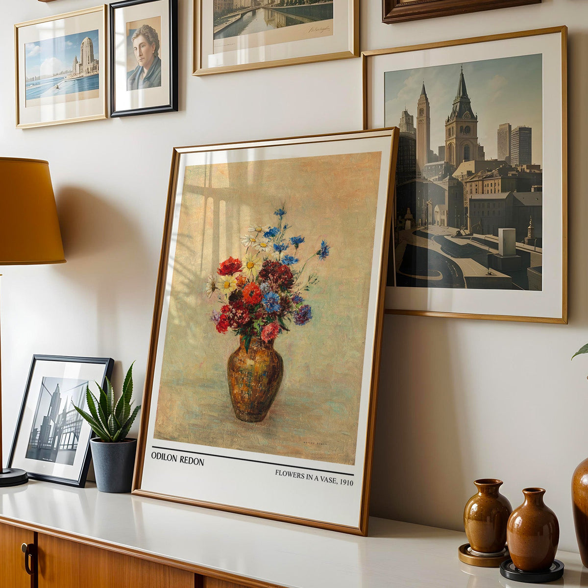 Botanical still life shown in a gold frame leaning on a sideboard in a gallery wall