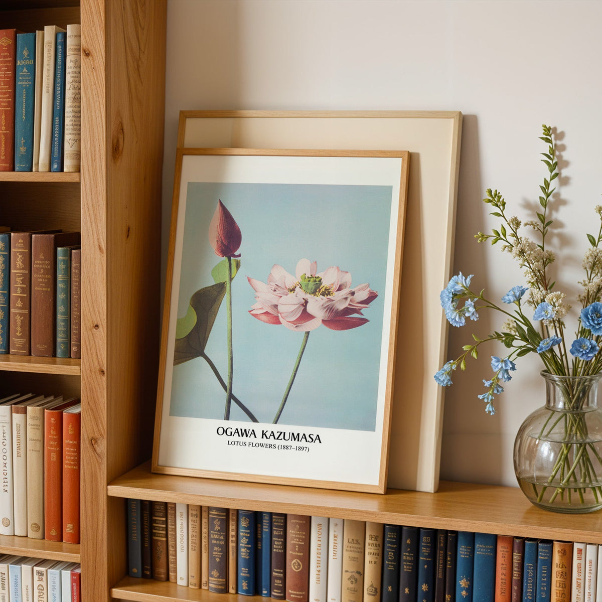 Botanical lotus print in an oak frame leaning on a bookshelf beside flowers