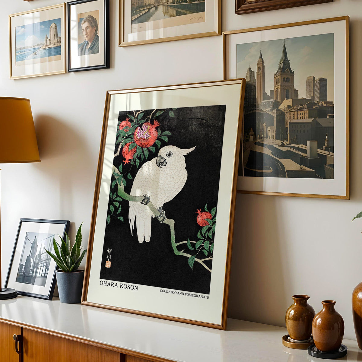 Koson bird print shown in a gold frame leaning on a sideboard in a gallery wall