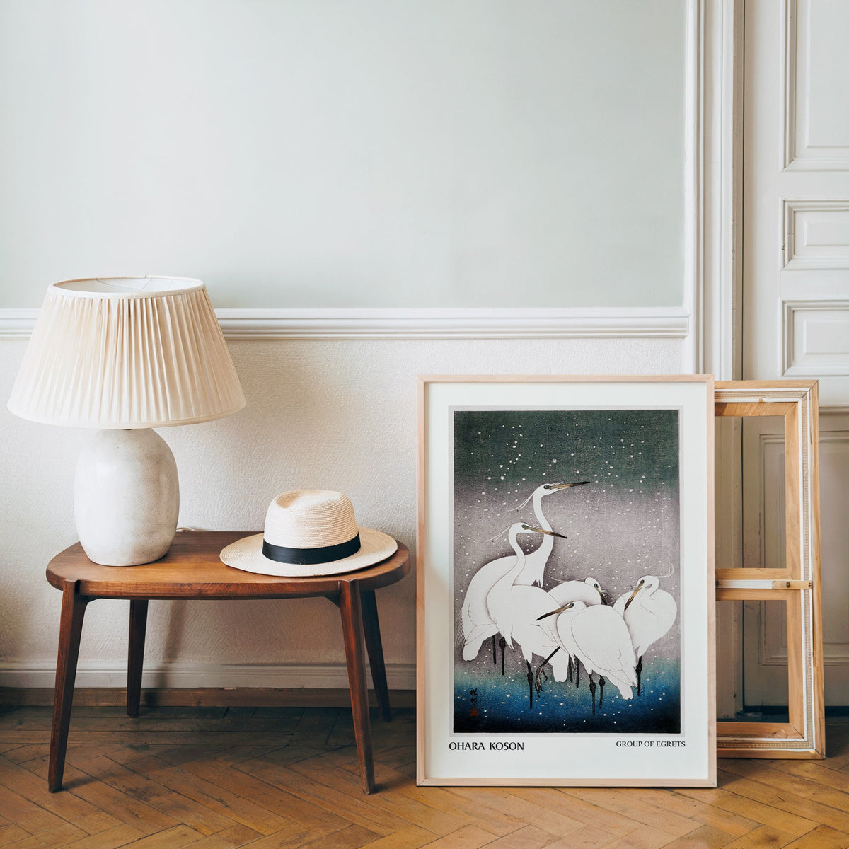 Snowy egret poster in a light wood frame leaning by a bench and panama hat