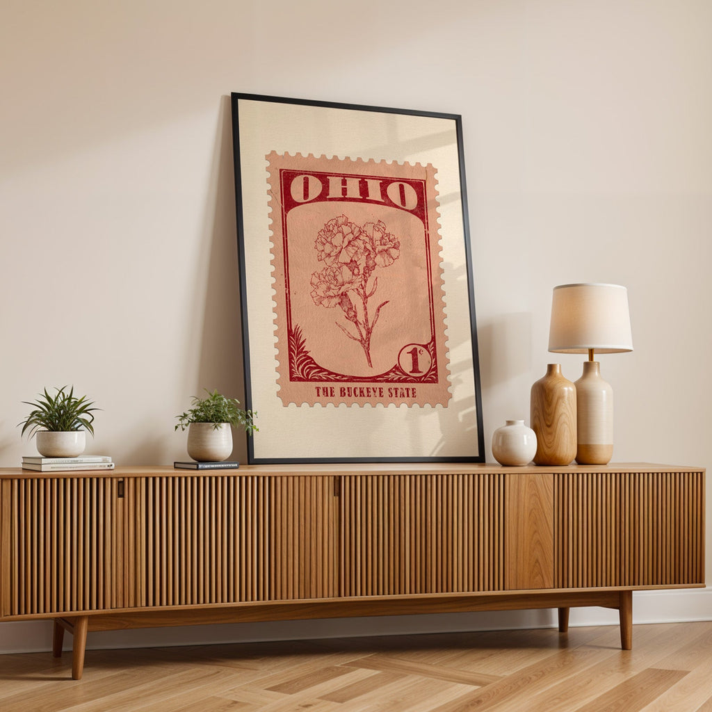 Ohio state flower print in a black frame leaning on a fluted wood credenza with vases and a lamp
