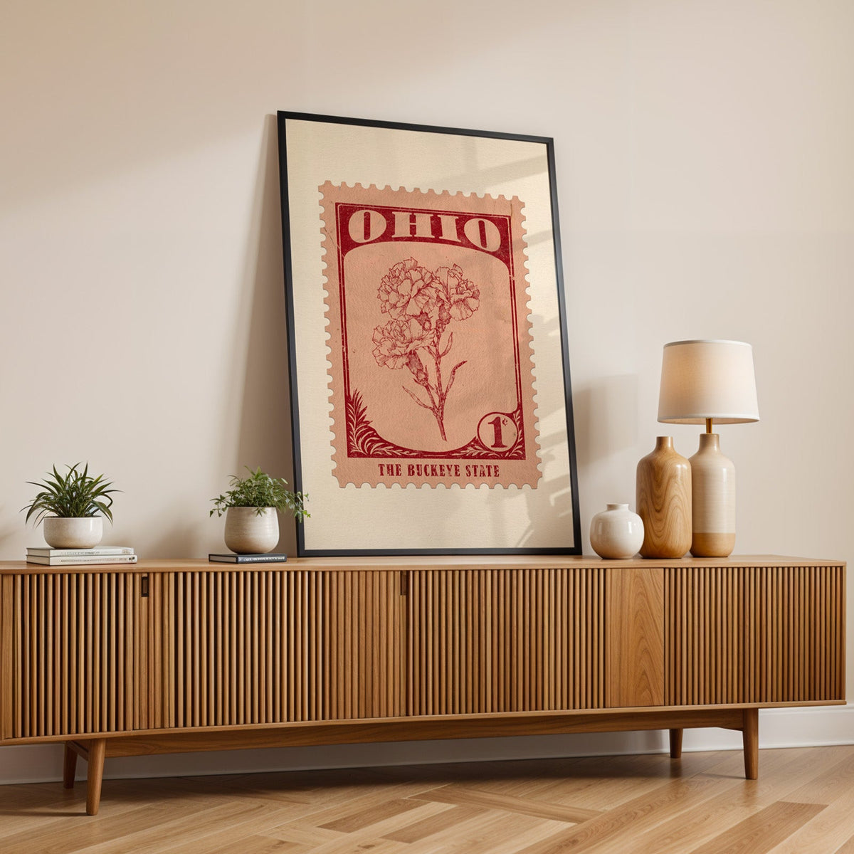 Ohio state flower print in a black frame leaning on a fluted wood credenza with vases and a lamp