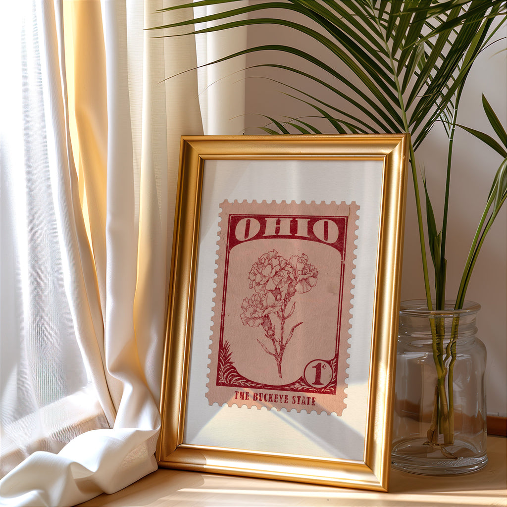 Ohio stamp print in a gold frame leaning by a cream curtain with a palm in a glass jar