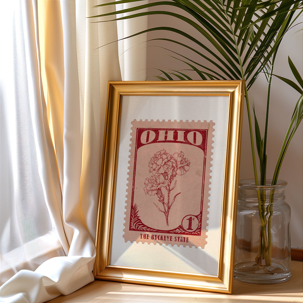 Ohio stamp print in a gold frame leaning by a cream curtain with a palm in a glass jar