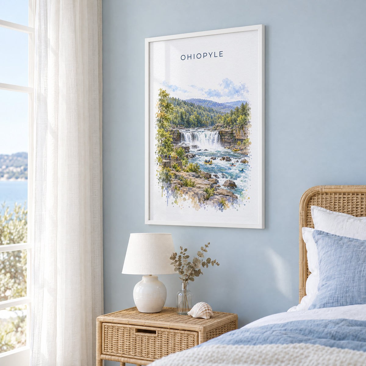 Ohiopyle State Park watercolor print in a white frame on a pale blue wall beside a rattan bed in a coastal bedroom