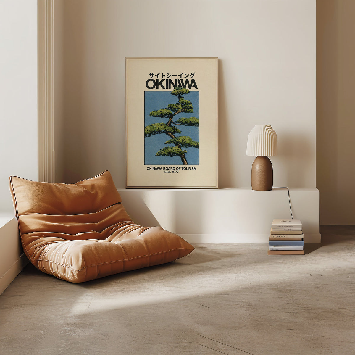 Okinawa pine tree travel poster print in a light oak frame on a white ledge by a tan leather floor chair