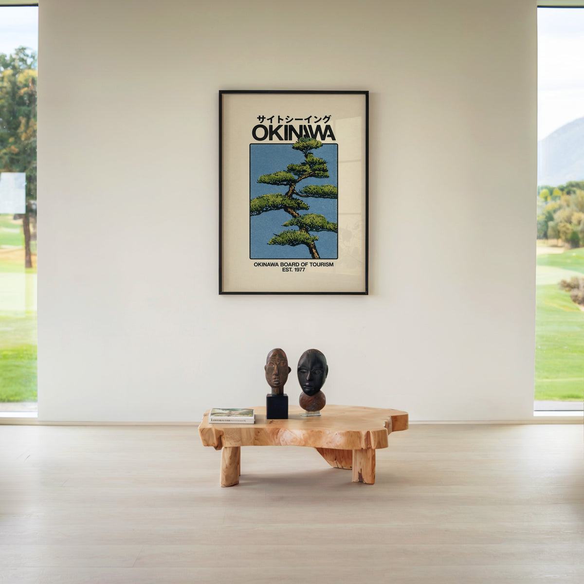 Okinawa pine tree travel poster print in a black frame above a live-edge wood coffee table between garden windows