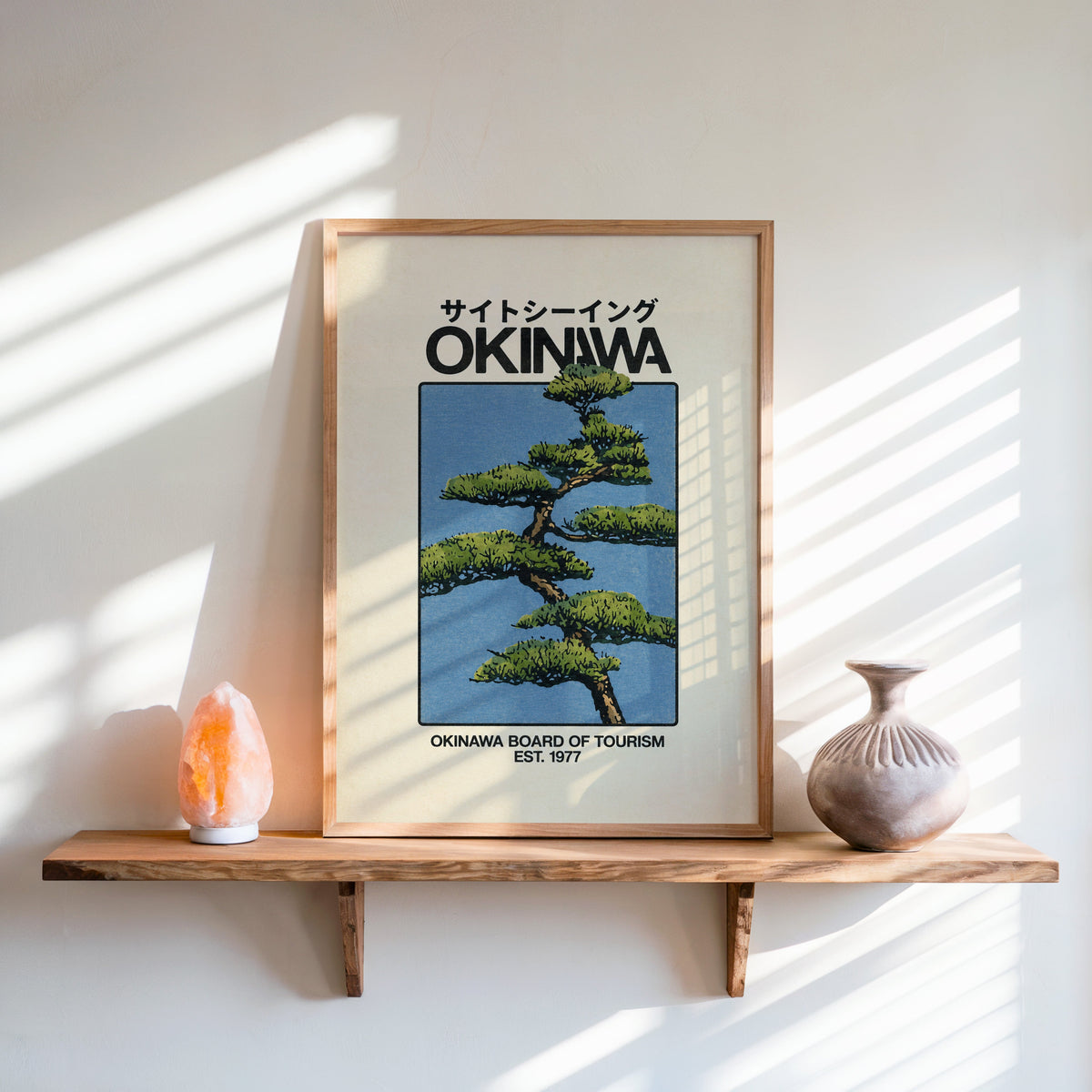 Okinawa pine tree travel poster print in an oak frame on a live-edge wall shelf with a salt lamp and clay vase