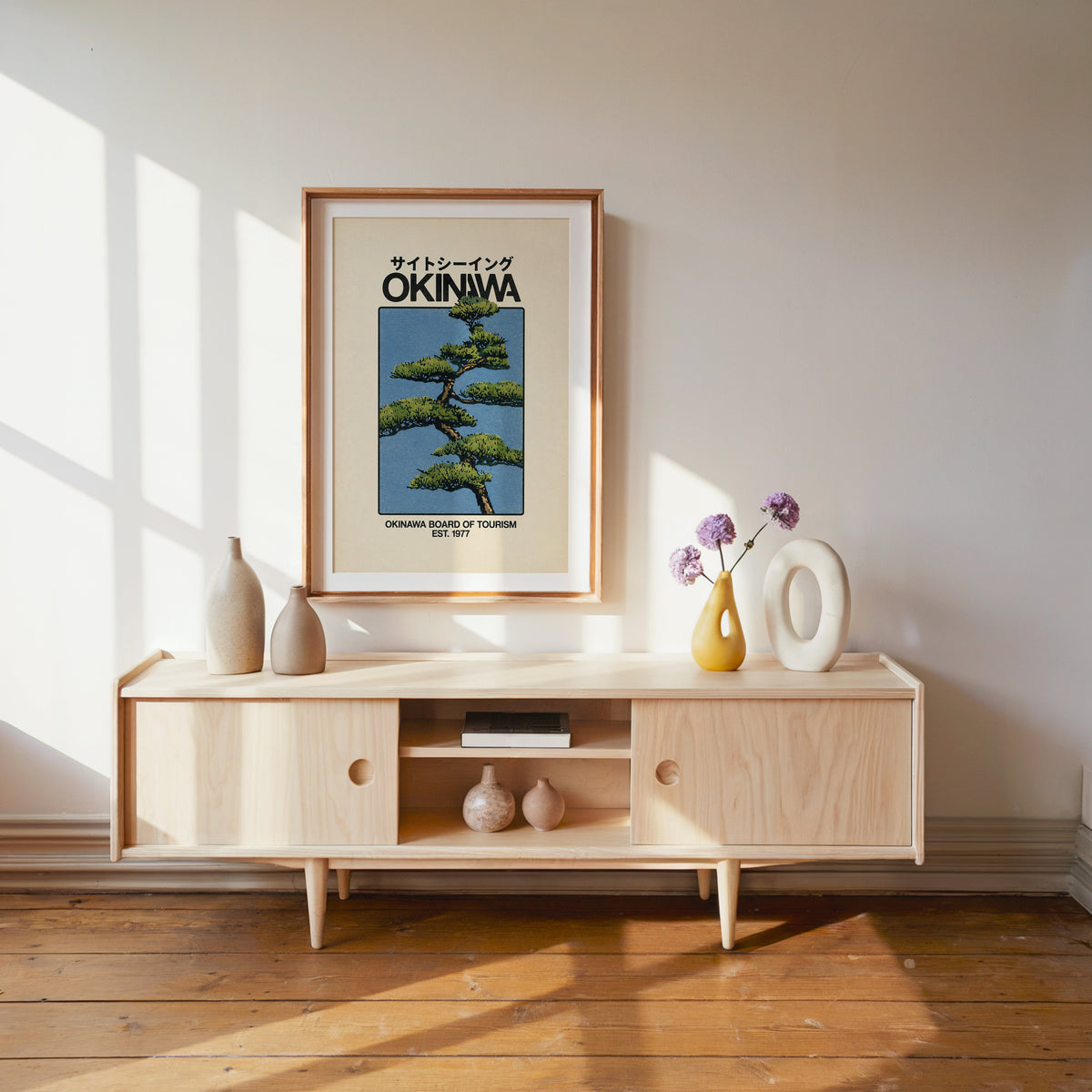 Okinawa pine tree travel poster print shown in a wood frame with a white mat above a pale wood media console