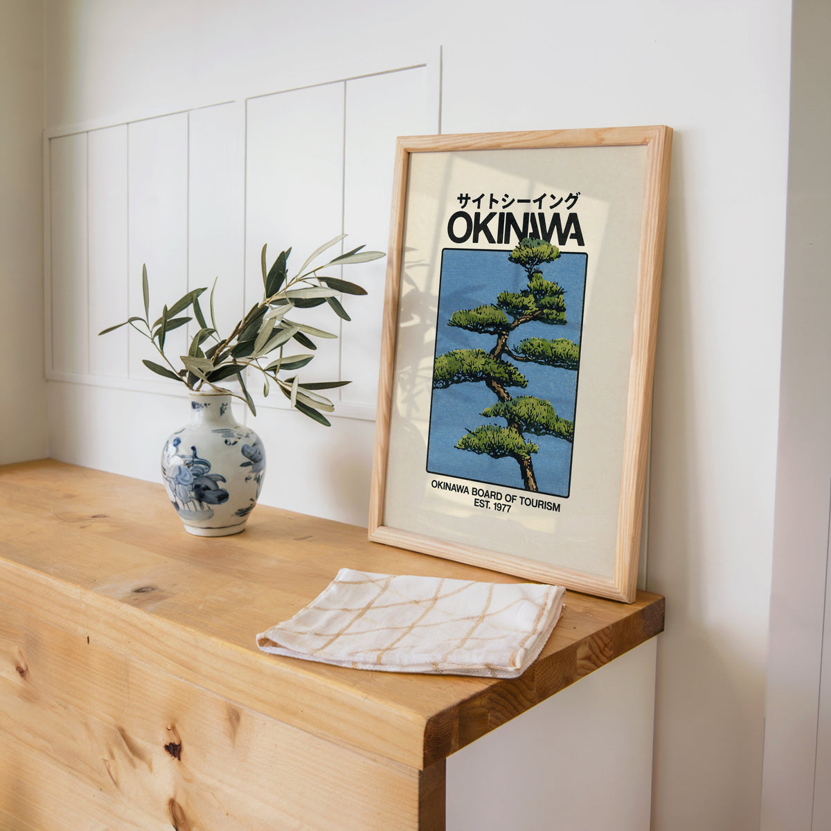Okinawa pine tree travel poster print in a pine frame on a wooden counter beside a blue and white porcelain vase