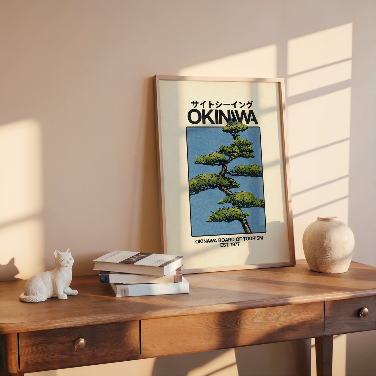 Okinawa pine tree travel poster print shown in a rose gold frame leaning on a wooden writing desk with books