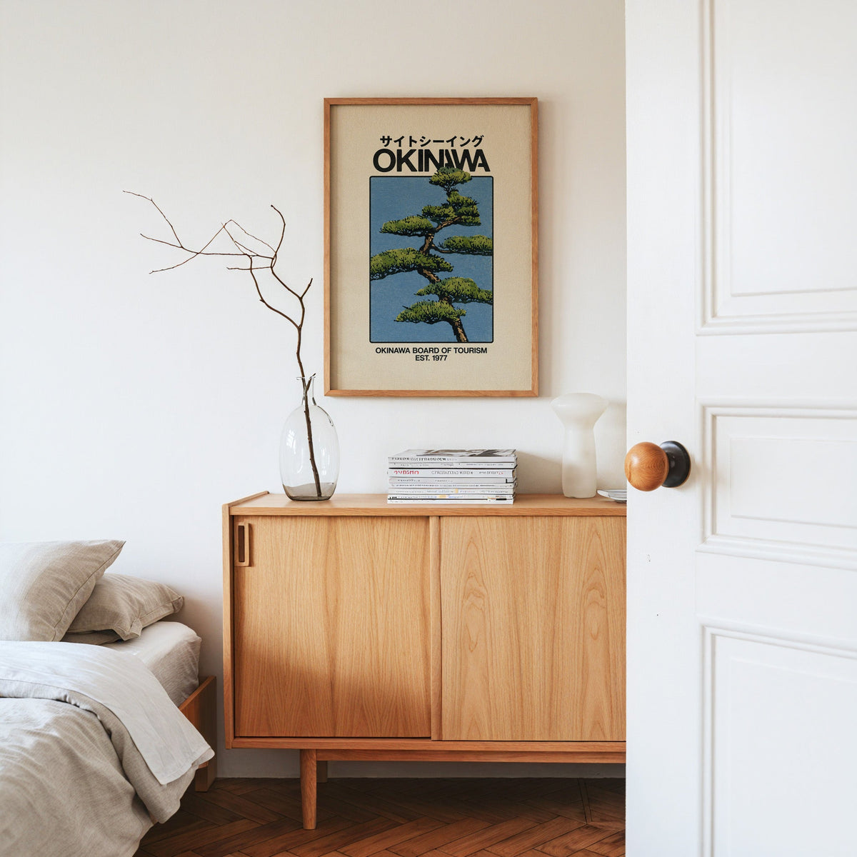 Okinawa pine tree travel poster print in an oak frame above an oak sideboard in a bedroom with linen bedding