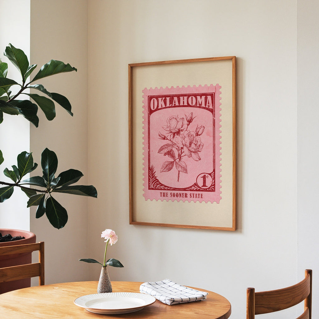 Oklahoma state flower print framed above a round wooden table with a single bloom in a vase and books