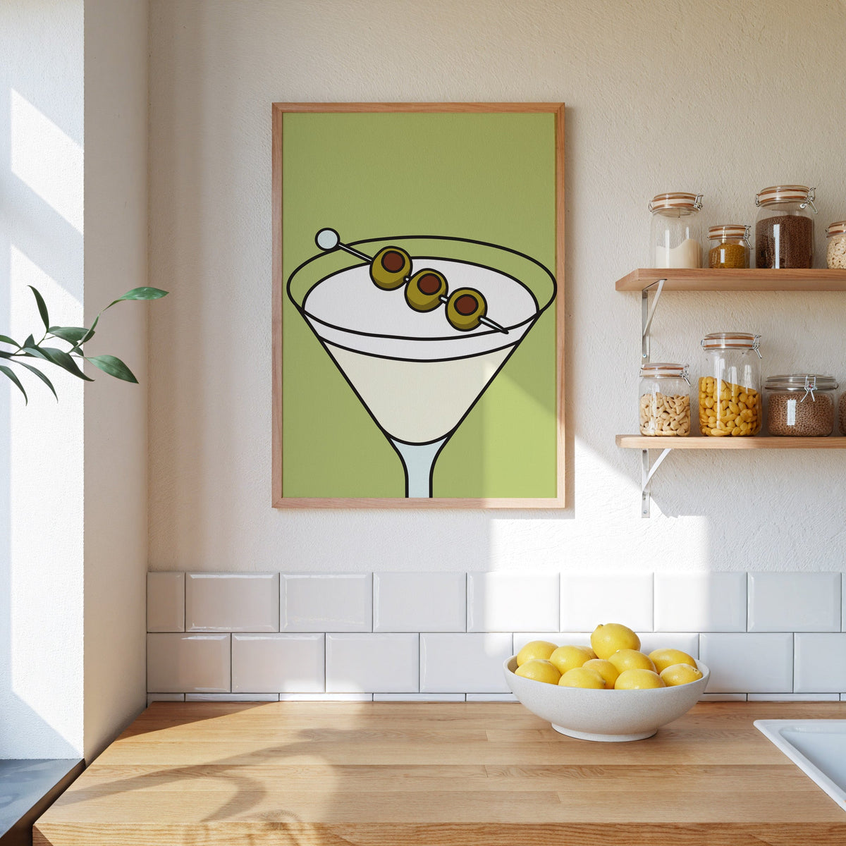 Olive martini green block print in an oak frame on a subway-tiled kitchen wall beside open shelves of pantry jars