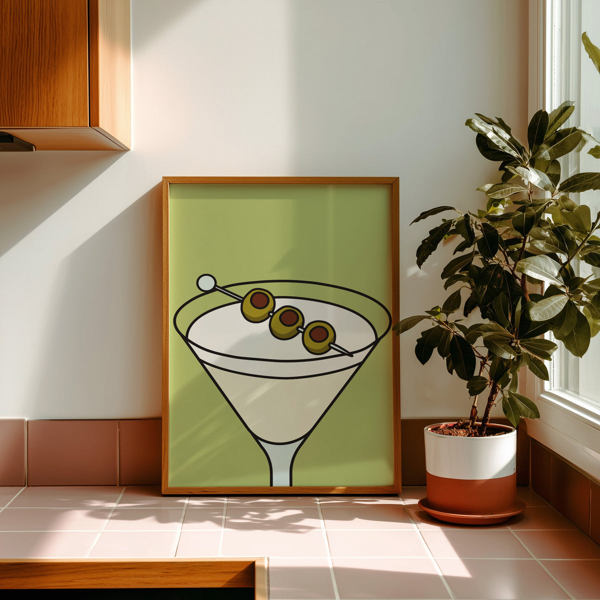 Olive martini green block print in a golden oak frame leaning on a pink tiled ledge in strong afternoon sun