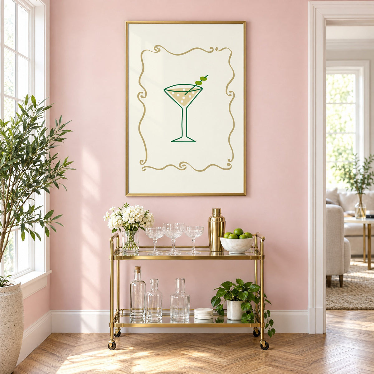 Olive martini in gold scroll frame print in a brass frame on a blush pink wall above a gold bar cart with glassware