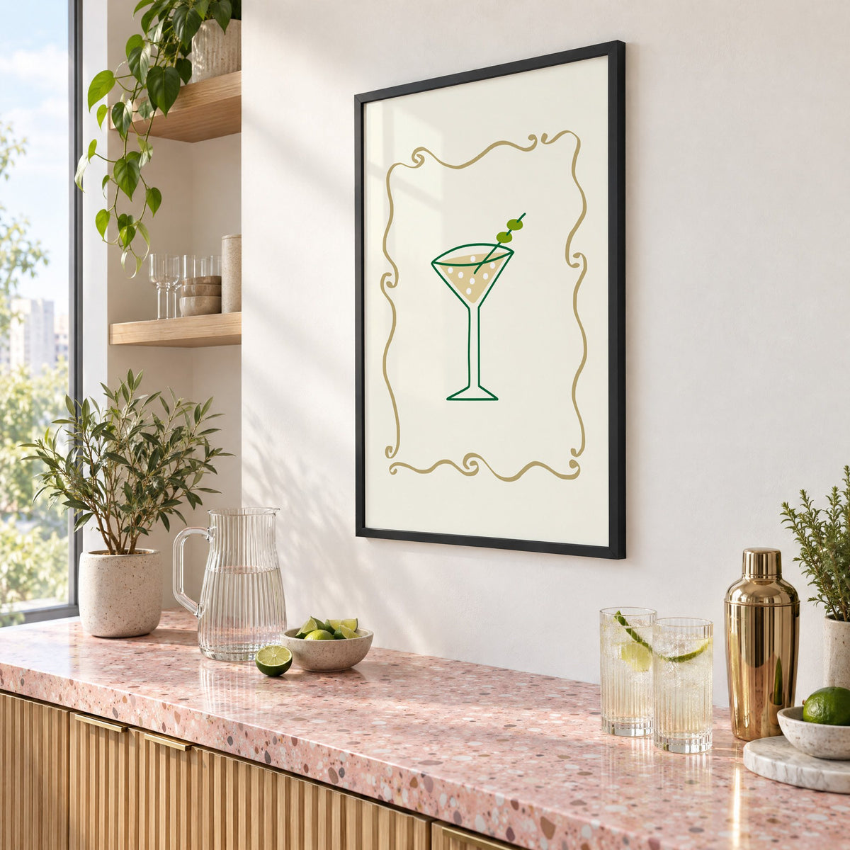 Olive martini in gold scroll frame print in a black frame above a pink terrazzo cocktail counter with limes, seen at an angle